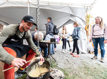 A food exhibitor at his booth and a festival-goer watching him.