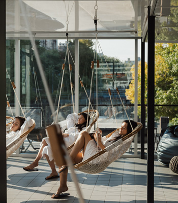 3 young women on the patio at the spa relaxing in hanging swing-chairs.