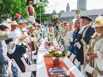 Guests in period costumes from the 17th century around a long dining table.