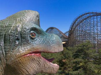 Close-up of a dinosaur's head, with a roller coaster in the background.