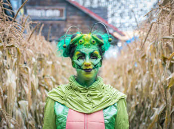 A woman wearing a green creature costume and make-up in a corn maze.