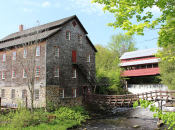 Exterior of the ancestral building, with a small wooden bridge over a stream.