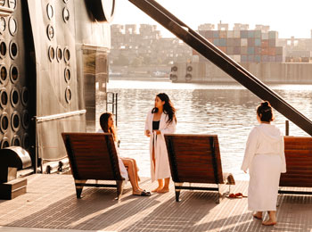 Three women in bathrobes on the spa terrace overlooking the water.