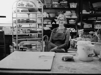 Ceramics artisan in her workshop with pieces displayed all around her.