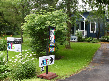 The outside of a quaint country house with a arts tour sign pointing toward it