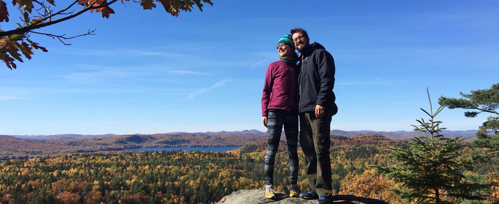 Two people posing on a rock in front of a fall landscape.