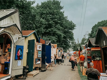 An alleyway lined with small cabins showcasing works of art.