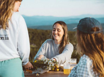 Three yound women around a table, with mountains in the background.