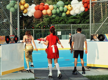 Three people on roller skates preparing to enter a rink decorated with balloons.